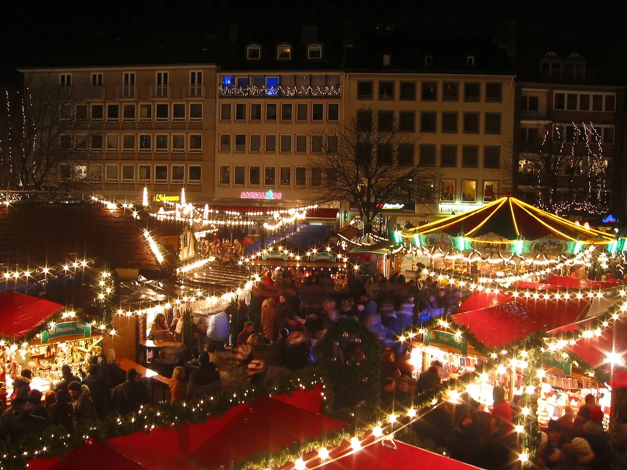 Marché de Noël illuminé sur la place du Marché d'Aix-la-Chapelle le soir, avec chalets, guirlandes et promeneurs